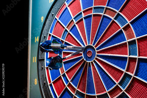 Close-up of three soft-tip darts hitting the segments of a blue and red electronic dart machine with focused lighting.