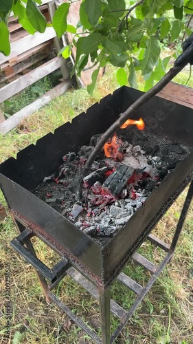 A person uses a stick to adjust red-hot coals in a barbecue grill outdoors. High quality 4k footage