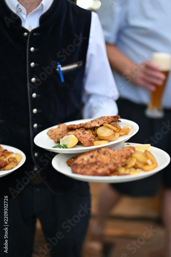 Schnitzel von einem Kellner in der Hand getragen im Biergarten in Tracht