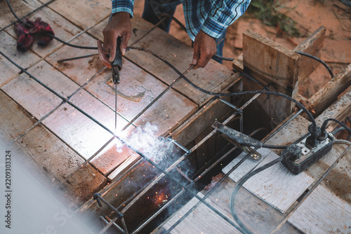 Professional Welder Using Electric Arc Torch on Steel Rebar Metal Frame Outdoors