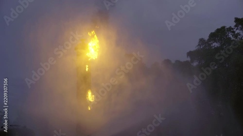 Massive fire blazing from factory chimney tower at twilight