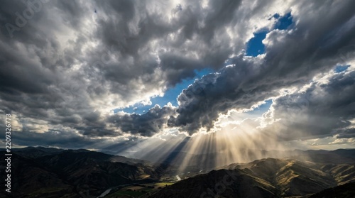 Powerful beams of sunlight breaking through dense gray-white storm clouds, dramatic sky photography, bright celestial rays, high contrast between silver clouds and blue openings, hopeful atmospheric