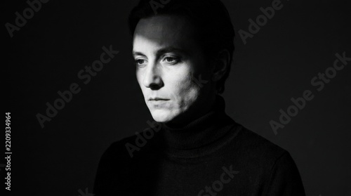 Shadowed human portrait emerging from near-black darkness, cinematic monochrome illustration, black turtleneck, single narrow light across face, strong chiaroscuro, introspective mood, minimalist