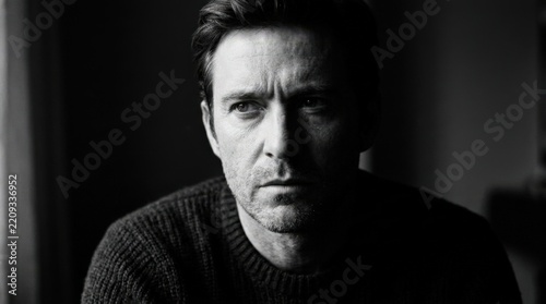 Partially cropped black-and-white male portrait with a serious expression emerging from deep shadow, cinematic monochrome photography, strong facial contrast, textured grayscale tones, minimal dark