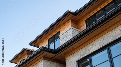 Modern luxury house exterior featuring natural wood siding and stone against clear sky.