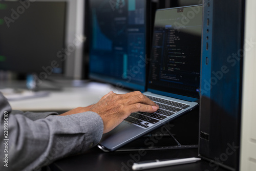 Close-up of a person typing code on a laptop beside server racks in a modern data center, cybersecurity, software development, and network management.