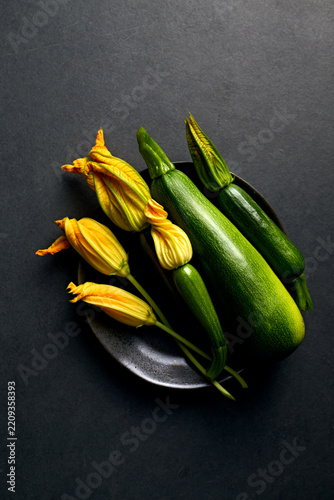 Fresh organic zucchini with yellow blossoms on a black plate