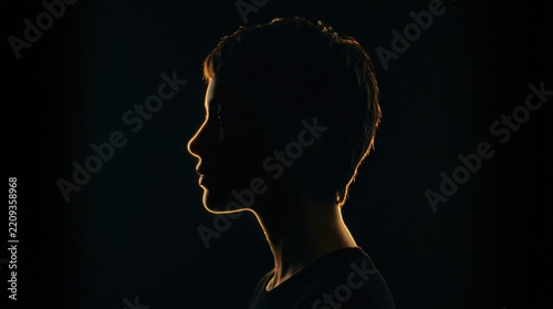 Human profile in near-black silhouette separated by a razor-thin golden rim light, cinematic portrait photography, deep black background, warm amber glow outlining nose and lips, dramatic minimal