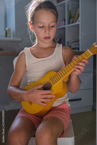 Little girl play small yellow guitar instrument in cozy home room scene