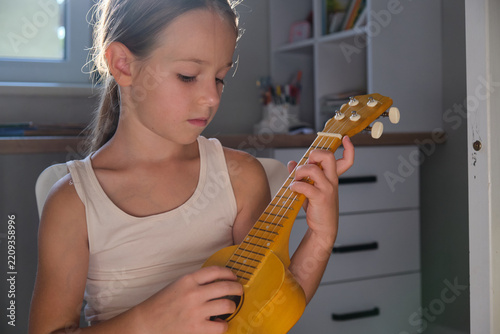 Little girl play small guitar in room at home for creative hobby art