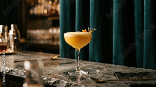 Elegant cocktail coupe filled with a frothy golden-orange drink on a gray stone surface, dark teal velvet curtains behind, luxury beverage photography, soft warm highlights, refined glass reflections,