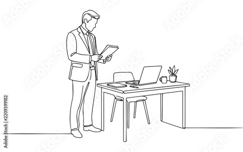 Business man standing and reading documents near a desk with a laptop and chair in a modern office environment