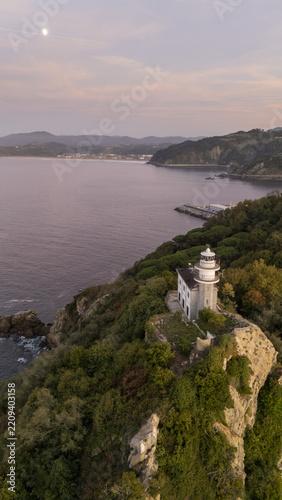 Aerial view of Getariako Itsasargia lighthouse perched on a rocky cliff overlooking the Bay of Biscay at sunset, with lush greenery and coastal scenery in Getaria, Euskadi, Spain.