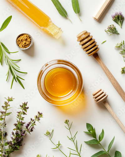 Top view of raw honey with herbal botanicals and wooden dippers on minimalist white background