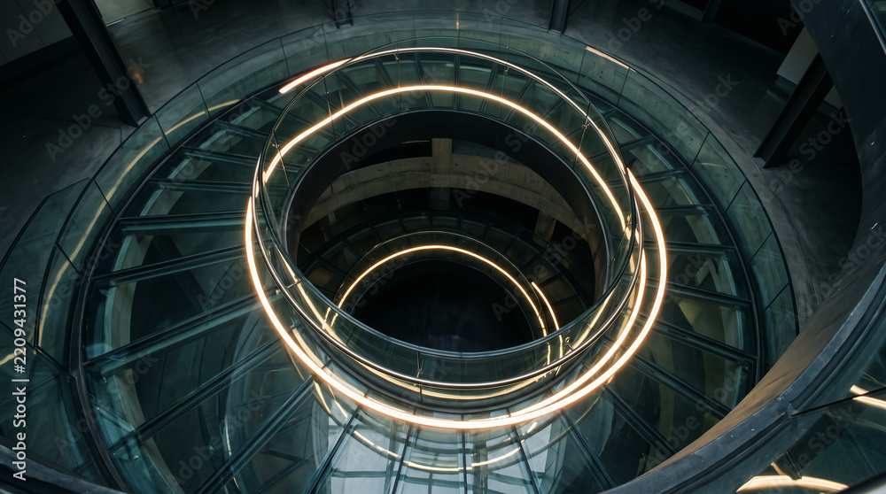 Fototapeta premium Modern spiral staircase interior with curved glowing handrails and layered architectural glass. Concept of luminous rails, illuminated handrail, modern architecture, circular stairs, glass railing.