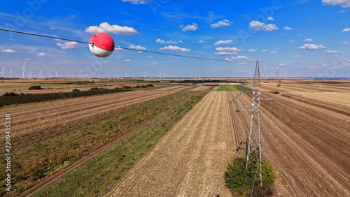 Aerial view of a signal ball on a transmission line with a pylon in a rural agricultural landscape with wind turbines in Bavaniste, Vojvodina, Serbia.