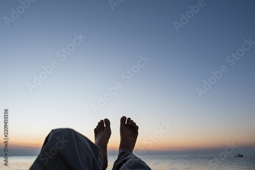First-person view of bare sandy feet relaxing on the beach facing the ocean at dawn.