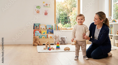 Toddler standing beside caregiver, happy child playing with education toy in nursery, smiling infant enjoying learning session with teacher