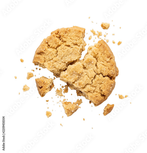 A single golden brown peanut butter cookie broken into pieces with scattered crumbs on white