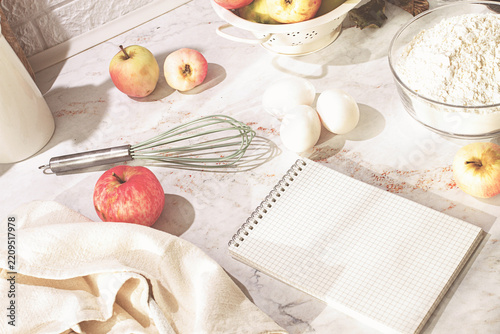 A bowl of apples, on the kitchen table, with baking ingredients, and a notebook, morning, no people,