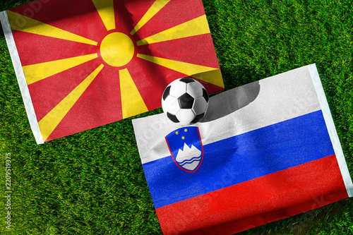 North Macedonia vs. Slovenia football match. National flags on green grass with soccer ball in the middle. Football background for international match.