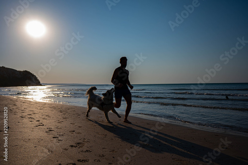 Man running with dog on beach at sunset