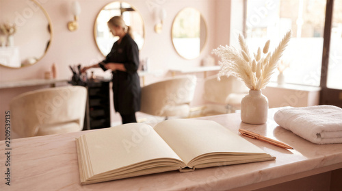 Open notebook on a marble reception desk in a modern aesthetic hair salon with a stylist working in the blurred background
