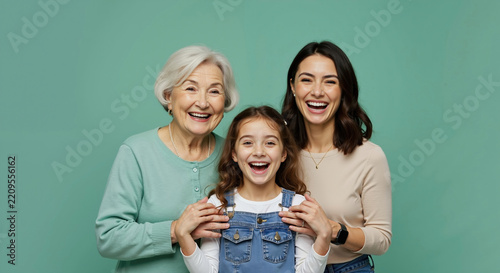 Three generations of caucasian women smiling at camera. Grandmother, mother and daughter standing together on green background. Multi-generational family bonding concept