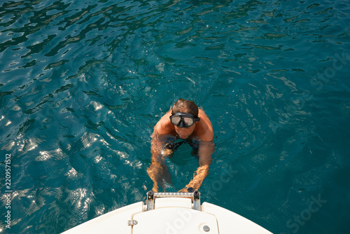 Man with diving goggles climb onto boat from sea