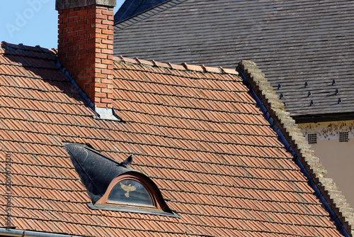 Close-up of an old tiled roof with a brick chimney and a small dormer window