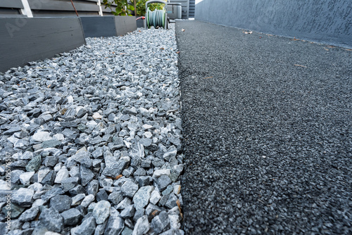 Closeup of crushed rock pathway bordered by dark rubberized gravel surface with raised planters and garden hose reel in background outdoor landscape hardscape texture