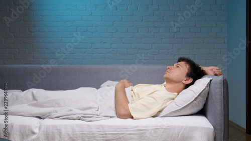 Young man lying awake in bed at night, staring at the ceiling, restless and anxious from insomnia and sleeplessness, struggling with stress, fatigue and quiet worry