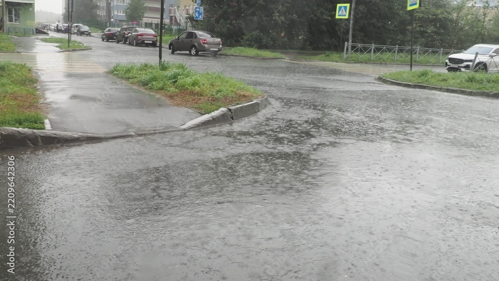 Fototapeta premium Puddles on the asphalt, rain falling, view from inside the car including the side mirror; a modern city in bad weather. drops of rain on the side window of the car water falls from the drivers windowb