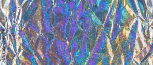 Crumpled holographic metallic foil texture with iridescent creases. Abstract shiny reflective background with rainbow gradient