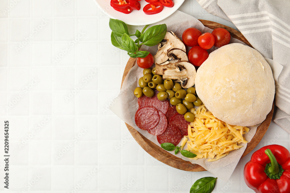 Fototapeta premium Making pizza. Dough and other different ingredients on white tiled table, top view. Space for text