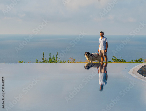 Man with dog overlooking the sea beside an infinity pool