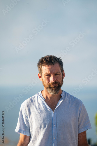 Bearded man standing outdoors with ocean in the background