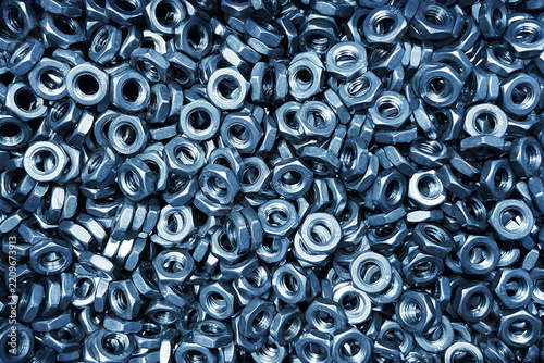 Pile of steel hexagonal nuts in close detail. Threaded metal fasteners and industrial hardware. Mechanical engineering background. Silver metallic nut texture with repeated geometric shapes.
