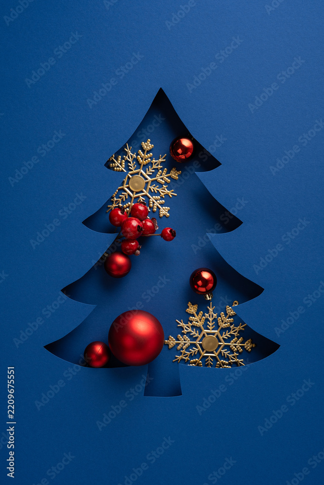 Fototapeta premium Merry Christmas and Happy New Year greeting with blue paper tree cutout and red ornaments on vertical blue background
