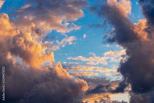 Dramatic clouds glow with warm golden light against a vivid blue sky, creating a majestic atmospheric sunset landscape.