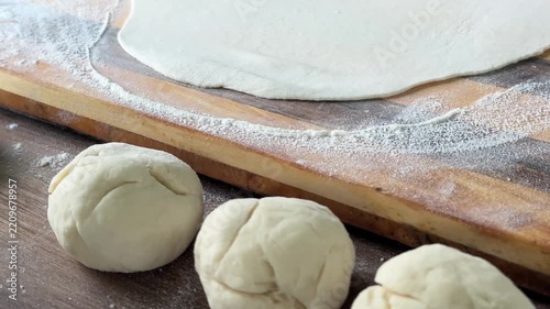 Close-up: balls of dough, a rolling pin rolls out lavash dough on a wooden board. High quality 4k footage