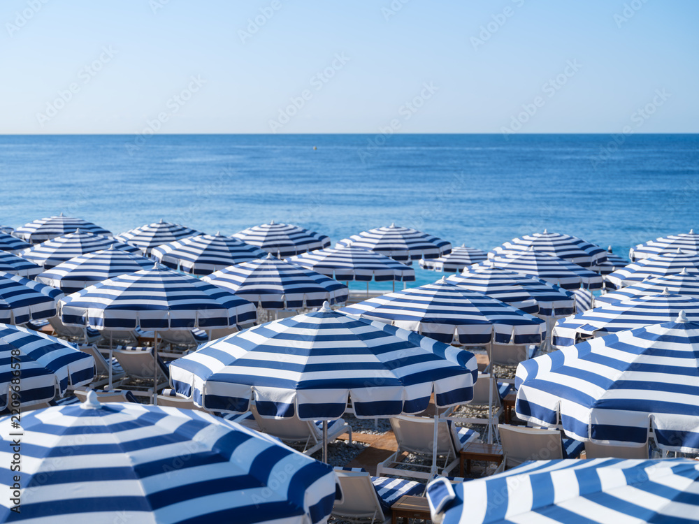 Naklejka premium Sun umbrellas and sunbeds on a sandy beach by the sea. Summer vacation and travel resort on a sunny day. A place to rest and relax.