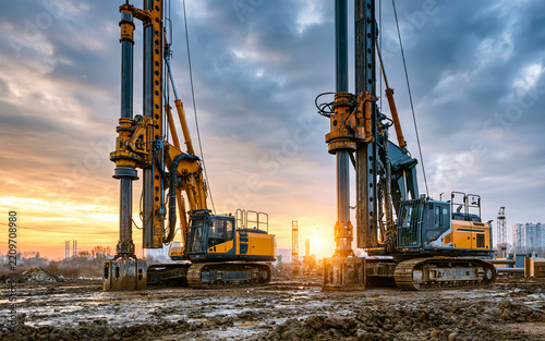 Two large drilling rigs standing ready on a construction site, symbolizing heavy industry, engineering, and foundation work