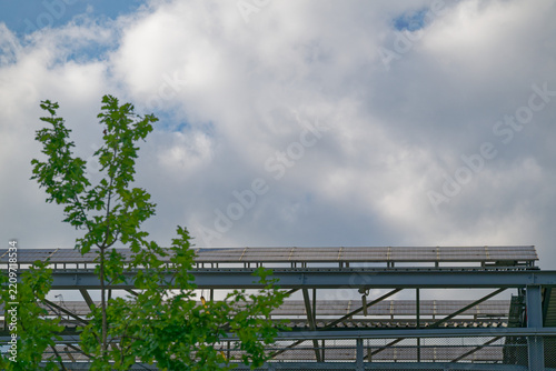 Solar panels installed on metal structure with green tree and cloudy sky background