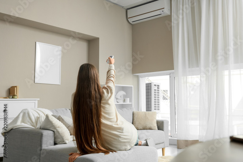 Energy efficiency and climate control, woman using air conditioner remote at ...