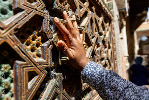 close-up view of a person's hand touching an intricately carved wooden screen, which is a classic piece of Islamic architectural latticework in Fes old town Morocco