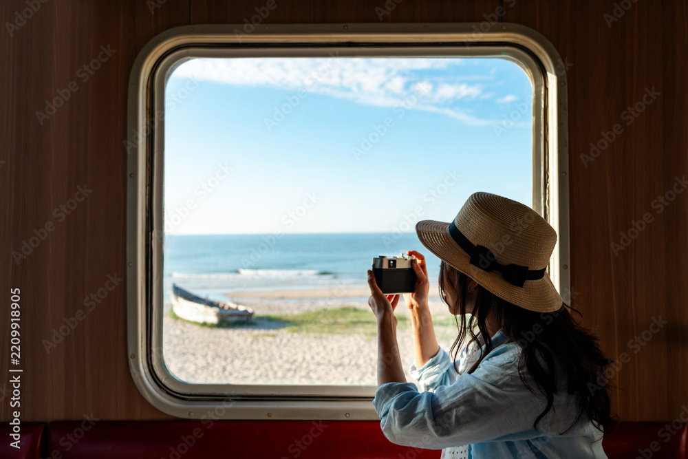 Fototapeta premium Solo female traveler taking pictures of sea view while traveling by train on summer vacation