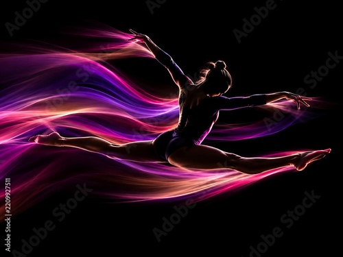 Female gymnast performing a graceful split leap in mid-air, surrounded by flowing purple and orange light trails against a solid black background, showing flexibility