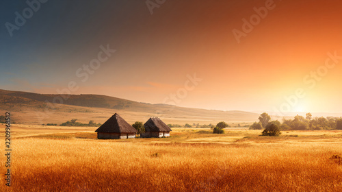 Rural landscape with golden fields and traditional straw huts under sunset sky
