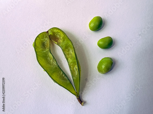 Fresh green boiled Edamame beans lie open on a plain white surface. Three round beans rest beside the pod. Natural, simple, and vibrant, they look fresh and healthy. Ideal for food, health